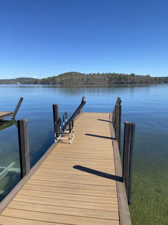 Brown composite dock with leaning posts and a swim ladder beside calm water