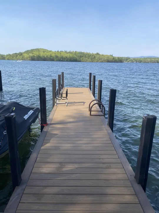 Finished brown dock extending between upright posts toward blue water and green wooded hills
