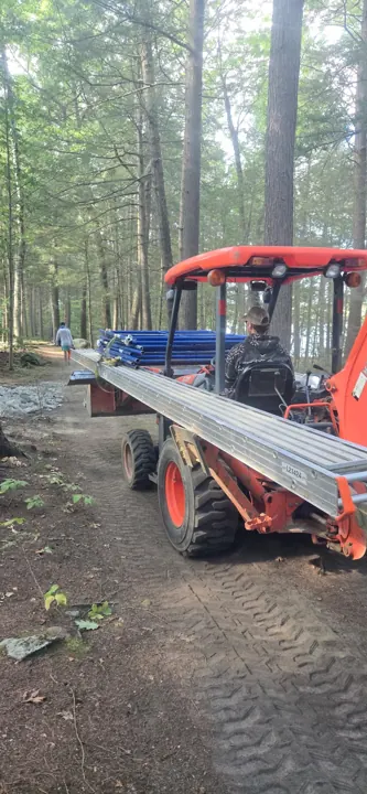 Tractor carrying staging through a wooded access path