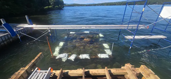 New crib footing visible through clear lake water below the staging