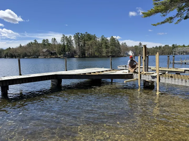 Worker in a red cap fitting new timber uprights beside exposed dock framing