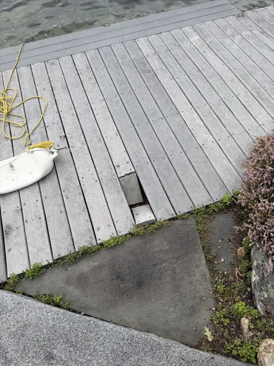 Close view of a dropped deck board at the shore end of a gray dock