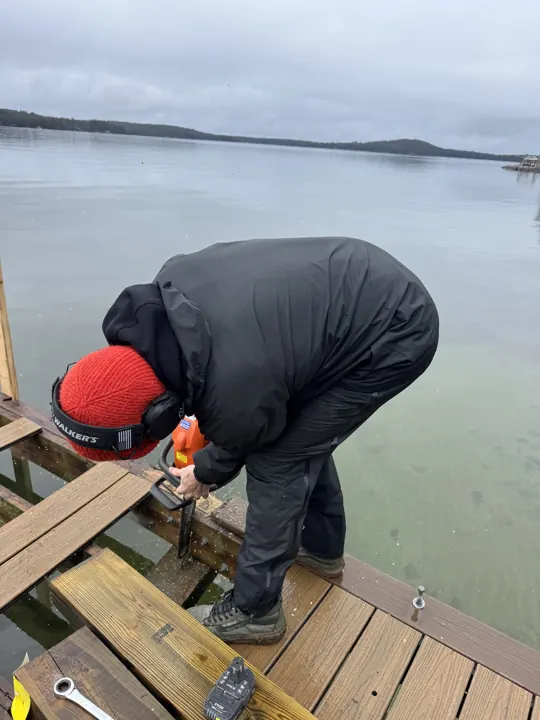 Worker in a red cap and hearing protection cutting dock framing in wet weather