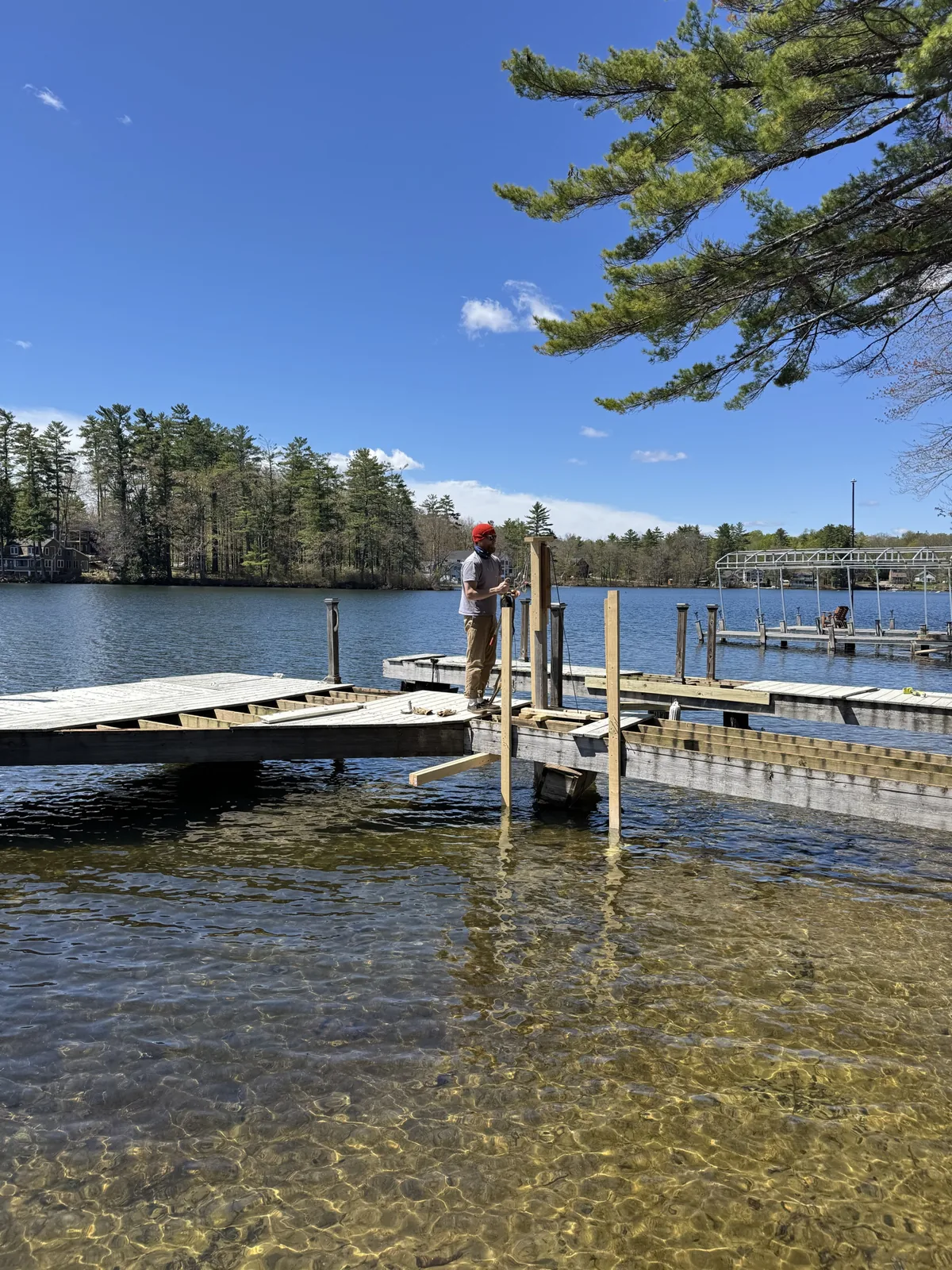 Worker in a red cap beside timber uprights over clear lake water
