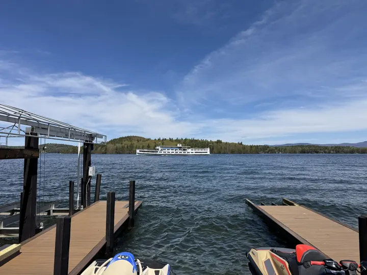 View between docks across Lake Winnipesaukee with a white passenger boat in the distance